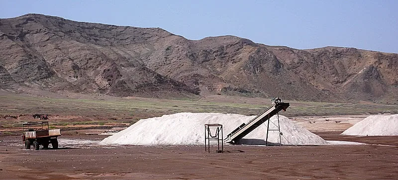 Montes de sal e equipamento transportador numa paisagem salineira